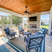 A screened in patio with a flat cedar ceiling and a fireplace.