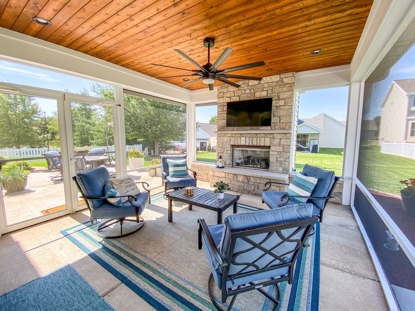 A screened in patio with a flat cedar ceiling and a fireplace.