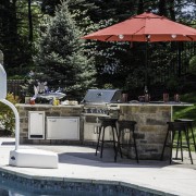 This poolside outdoor kitchen in Chesterfield has a masonry base, granite counter, bar height seating area, Napoleon grill, True outdoor refrigerator, storage and more!